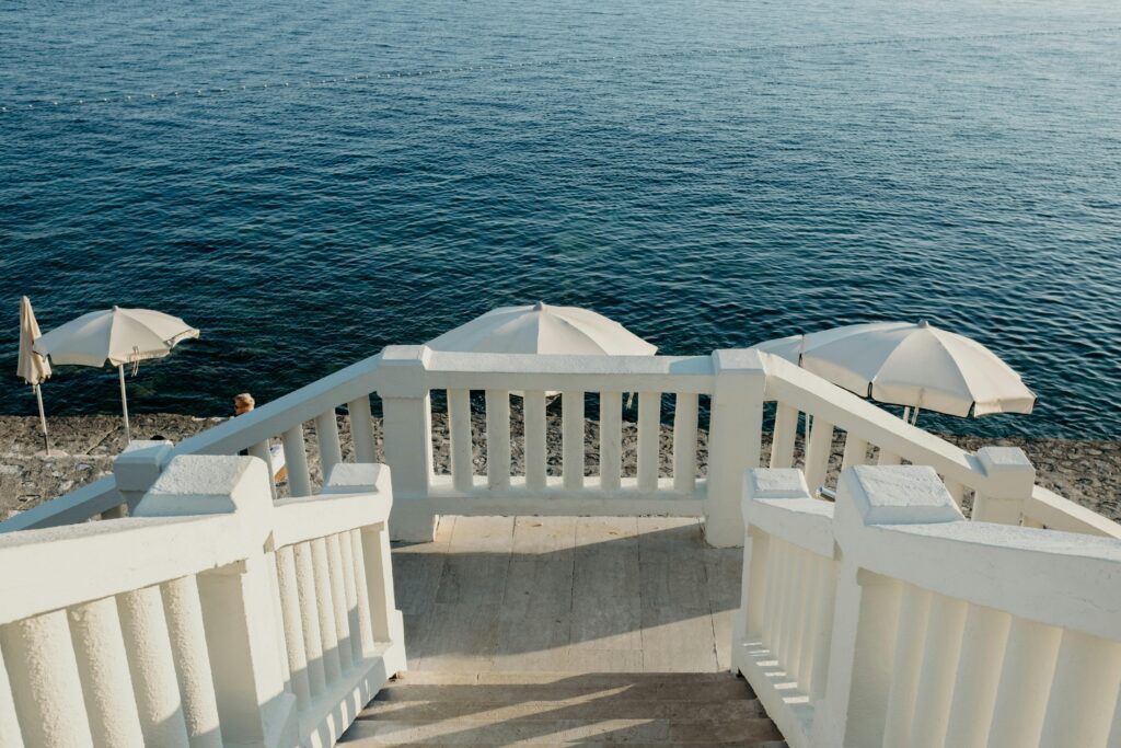 pexels-photo-16514419-16514419 Steps lead to a serene sea with umbrellas on a sunny day, evoking relaxation.