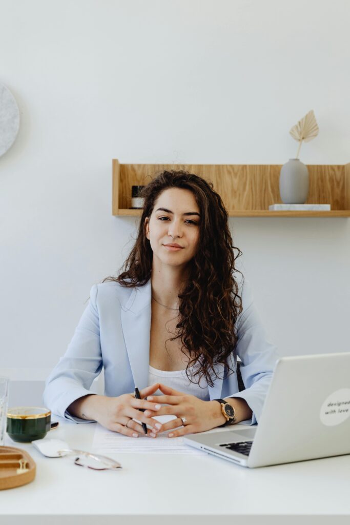Portrait of a confident businesswoman sitting at a desk with a laptop in a modern office.